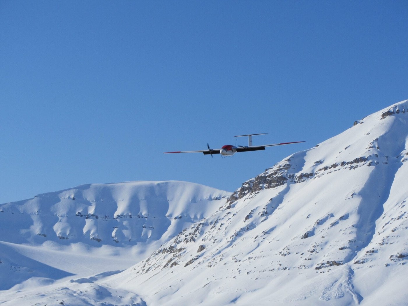 A fixed-wing research drone in flight past a snowy mountainside